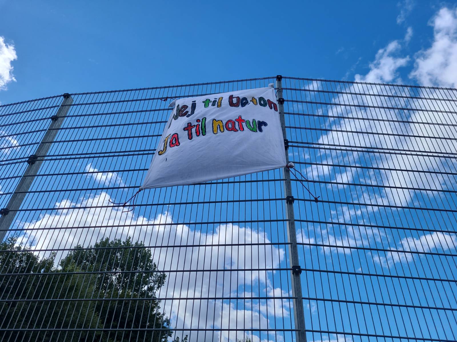 A banner on a fence with the text "Neg til beton, ja til natur!" or "No to concrete, yes to nature!"